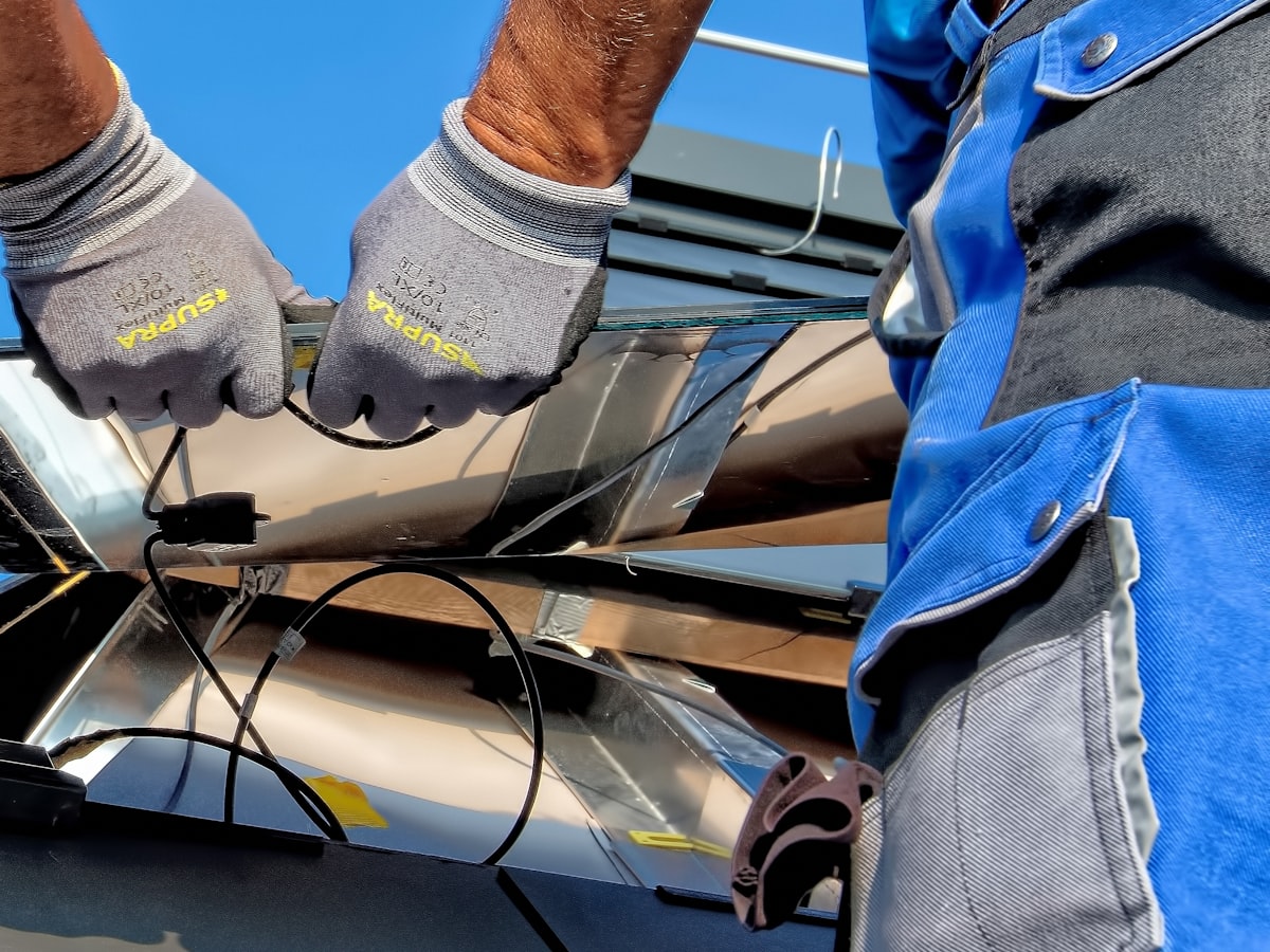 Male technician cleaning dust from rooftop solar panels with a soft-bristle brush and a hose